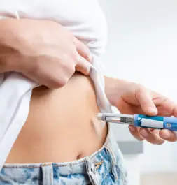 Close-up of a person administering a subcutaneous injection into the abdomen using an injector pen.
